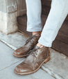 A man wearing a pair of brown Bed Stu Clyde lace up shoes.