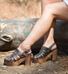 A woman is sitting on a log in a wooded area wearing Fontella by Bed Stu.