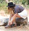 A woman tying her Fontella shoes by Bed Stu on a log.