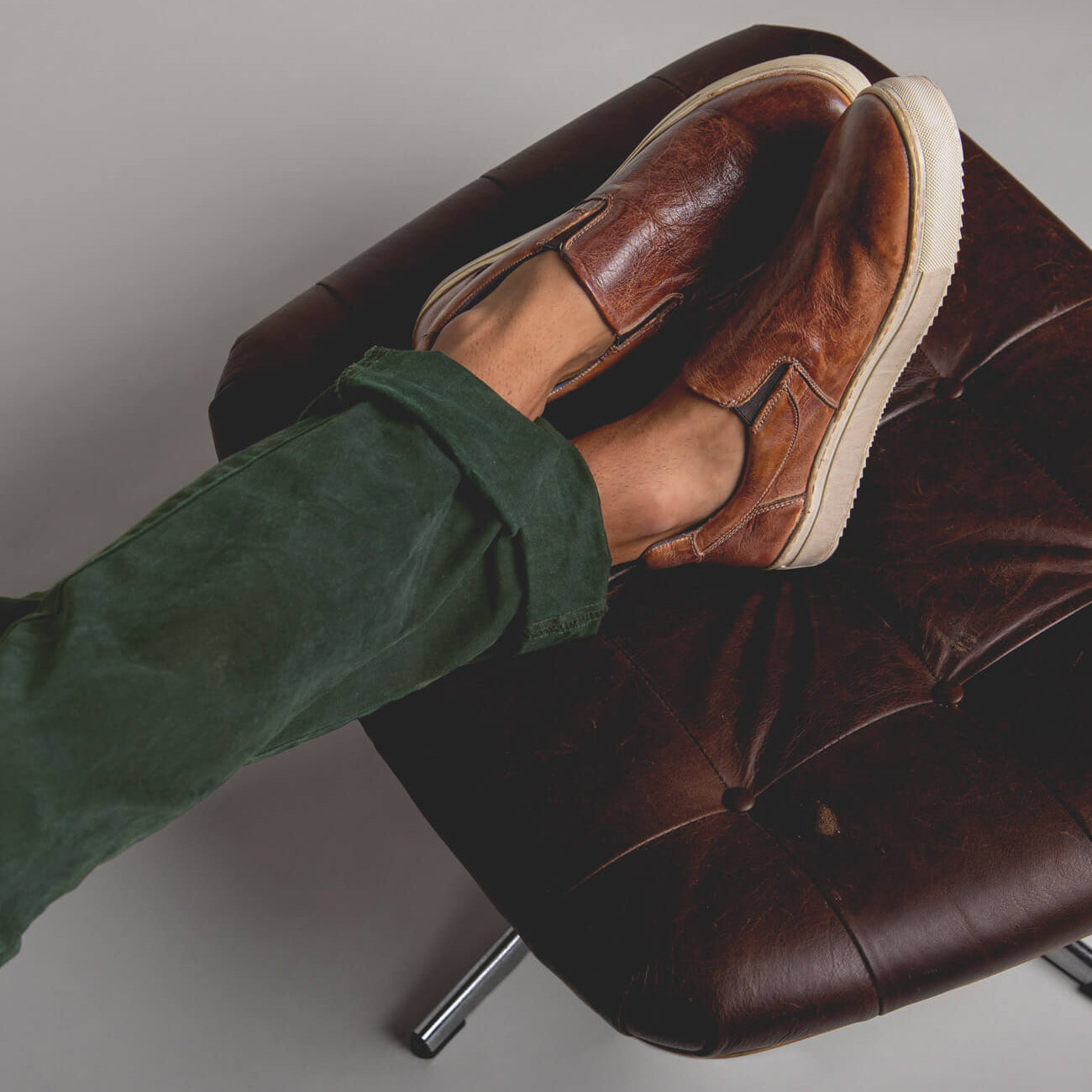 A person's feet sitting on a Harry leather chair.