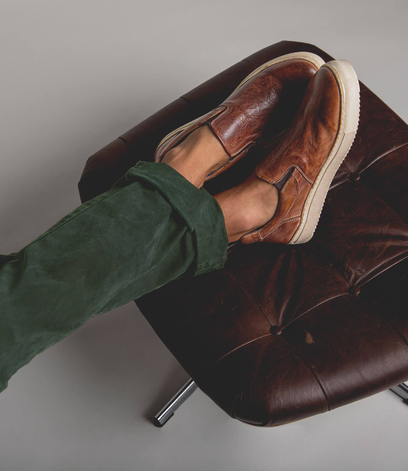 A person's feet sitting on a Harry leather chair.