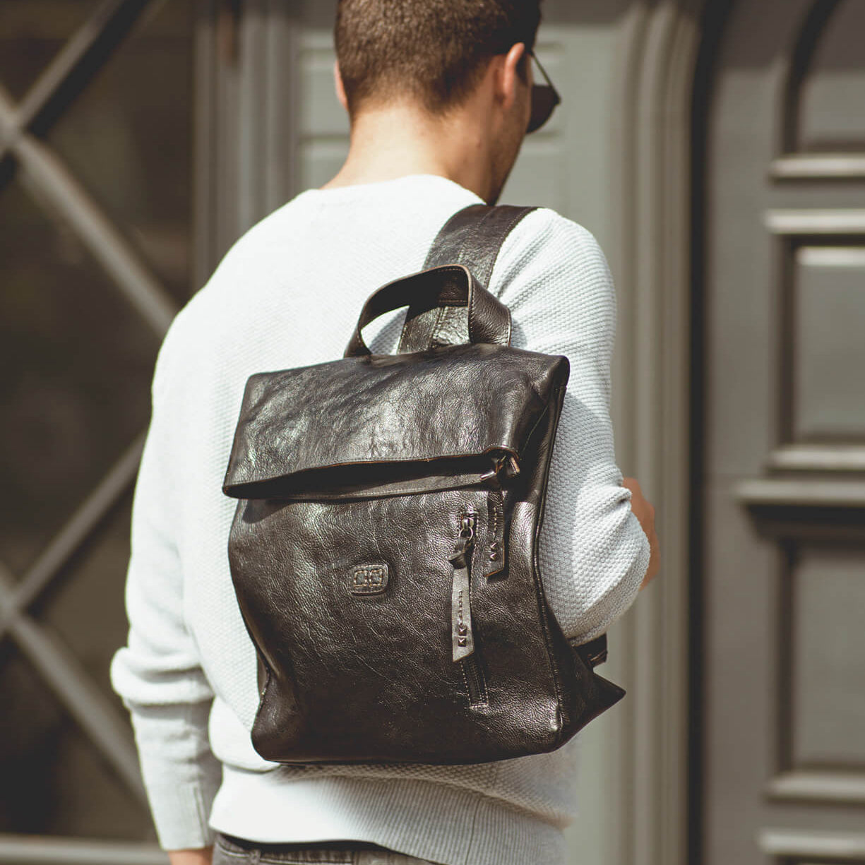 A man wearing a white shirt with a black Bed Stu Howie backpack.