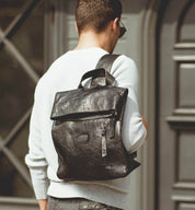 A man wearing a white shirt with a black Bed Stu Howie backpack.