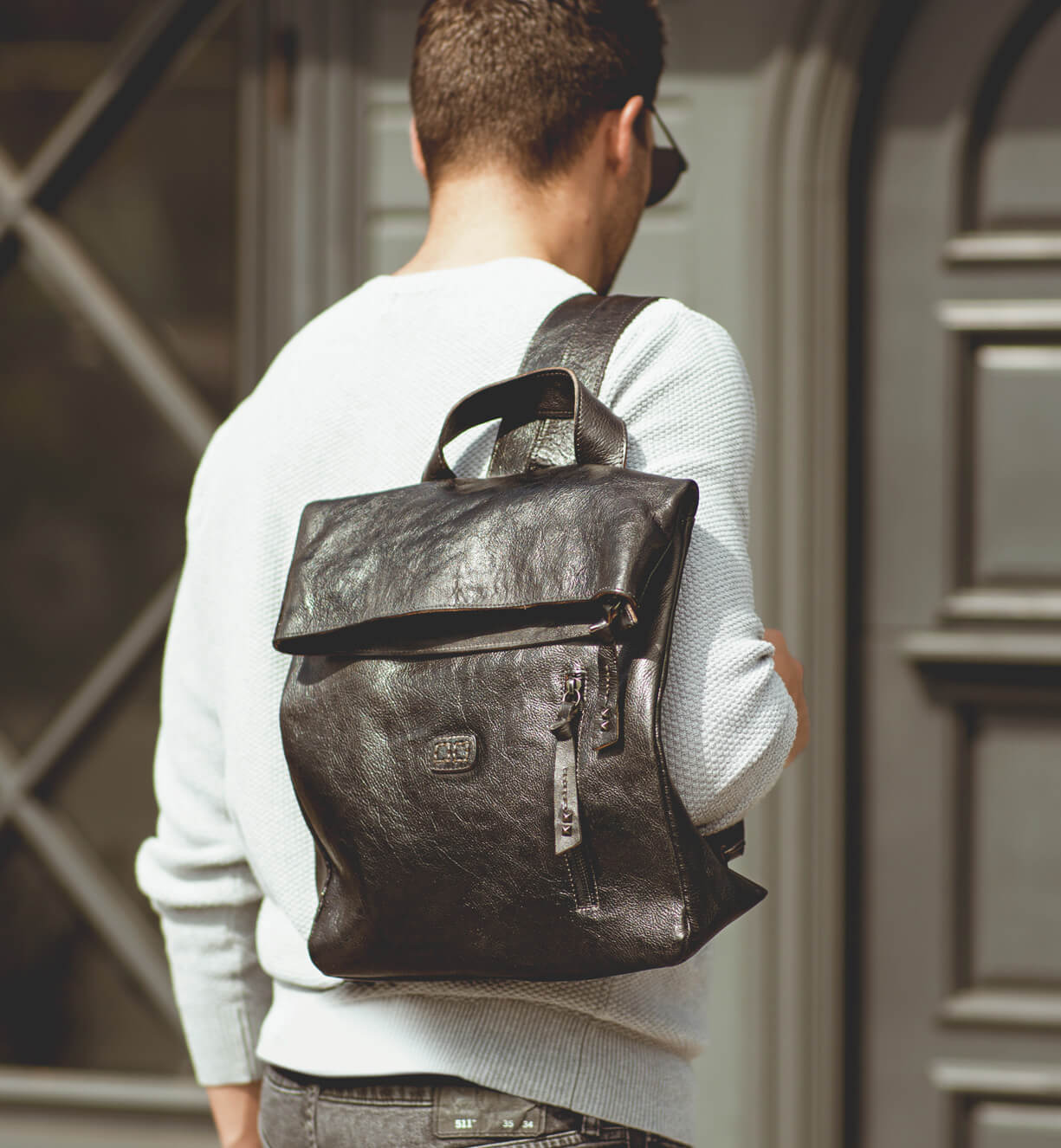 A man wearing a white shirt with a black Bed Stu Howie backpack.