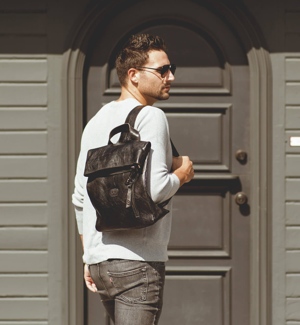 A man is standing wearing a black Bed Stu Howie backpack.
