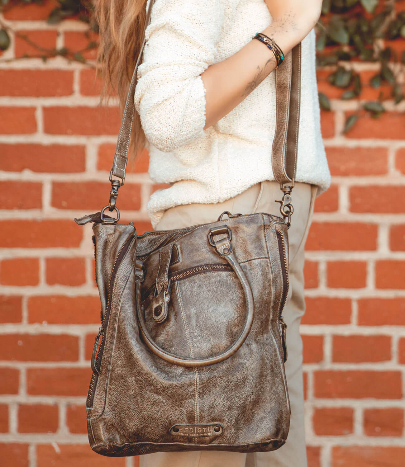 A woman holding a Bed Stu Mildred handbag in front of a brick wall.
