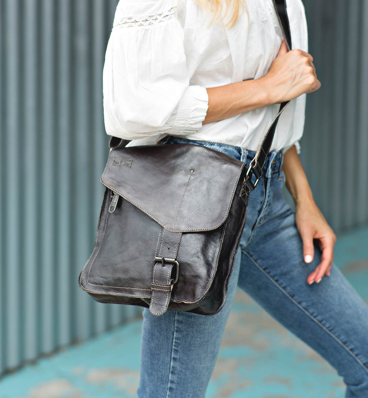 A woman wearing a white shirt and jeans holding a Bed Stu Venice Beach black leather bag.