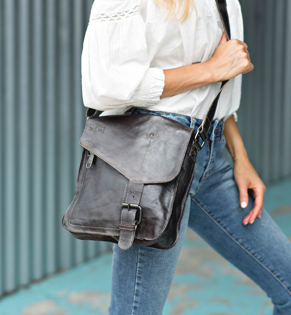 A woman wearing a white shirt and jeans holding a Bed Stu Venice Beach black leather bag.