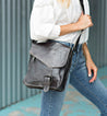 A woman wearing a white shirt and jeans holding a Bed Stu Venice Beach black leather bag.