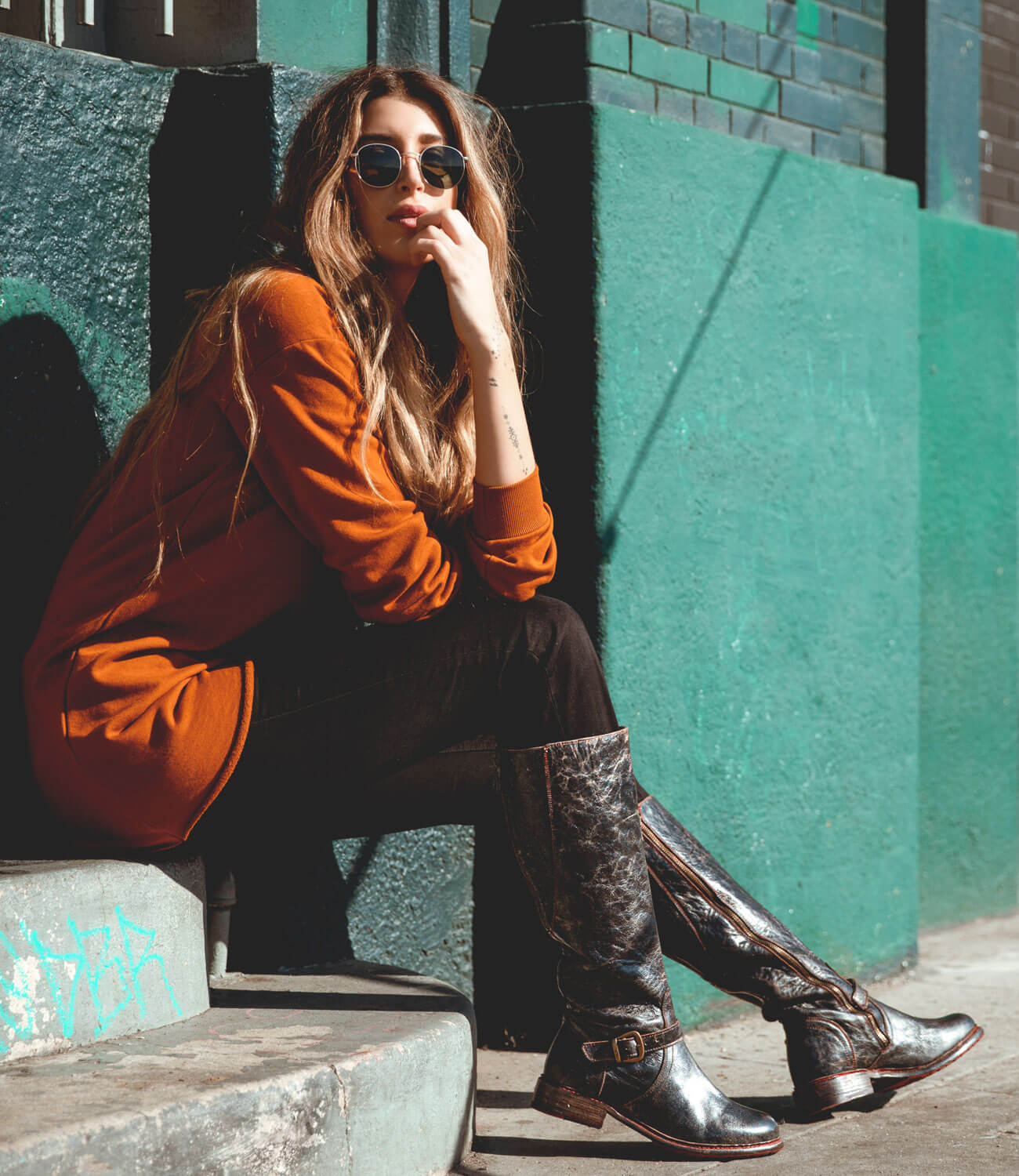 A woman is sitting on the steps of a Glaye building from Bed Stu.