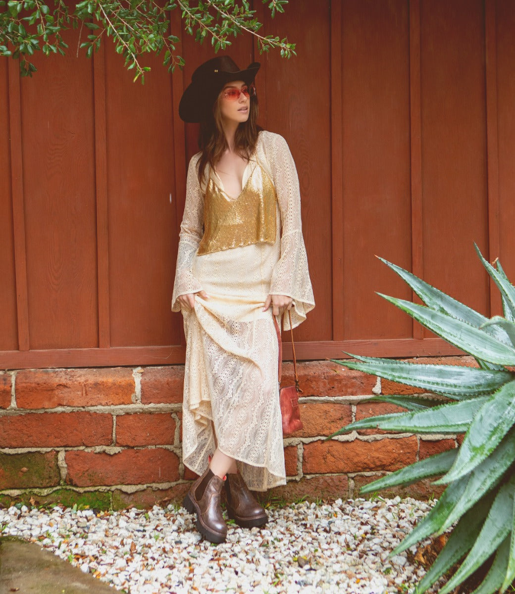 A woman in a cowboy hat and boots is standing in front of a wall wearing Valda Hi shoes by Bed Stu.