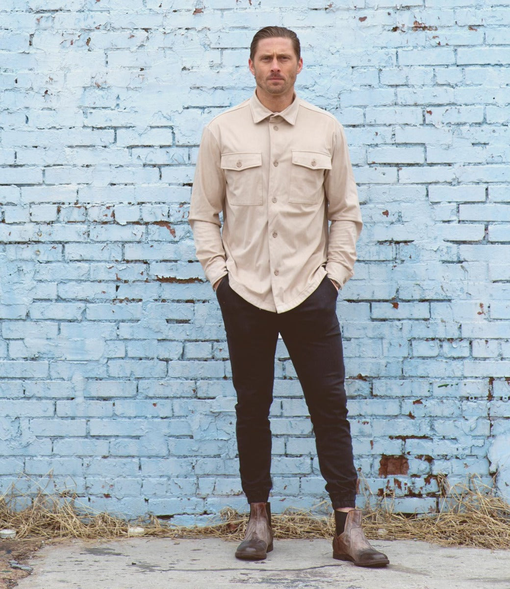 A man standing in front of a blue brick wall wearing a Bed Stu Vasari shirt.