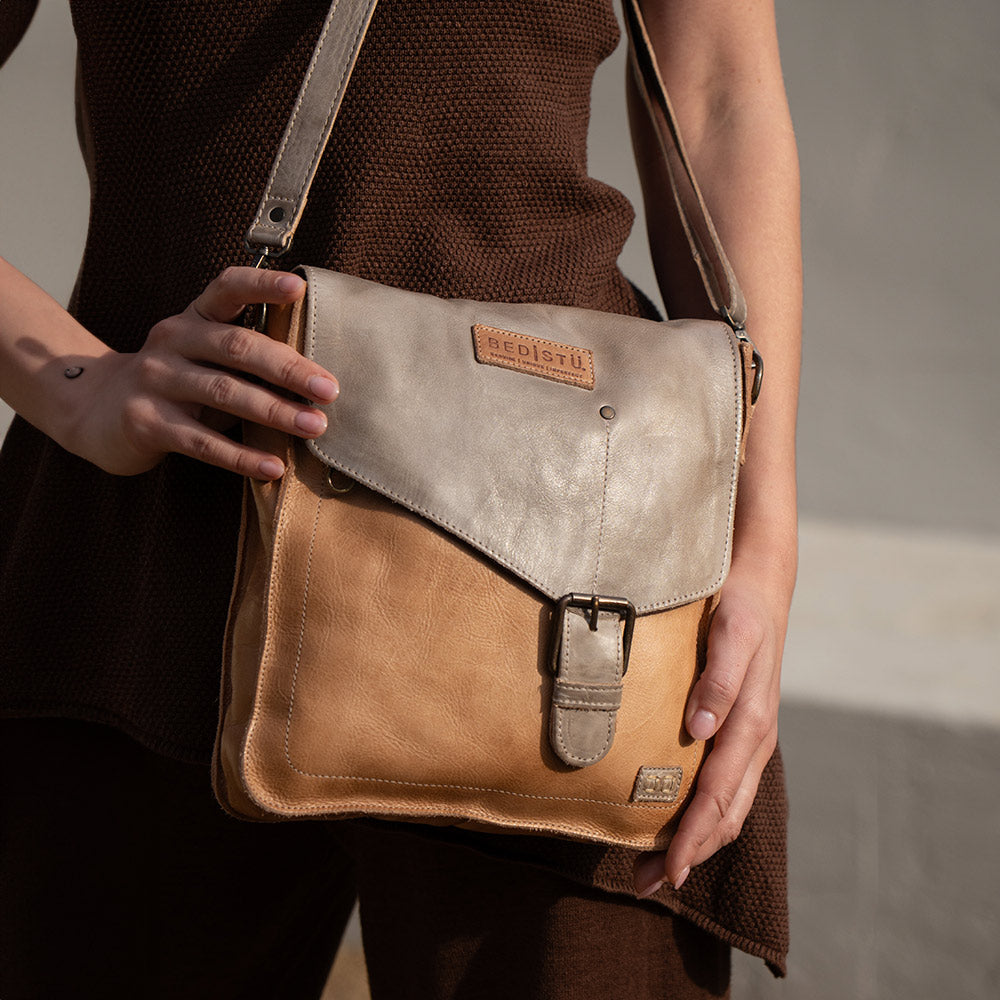 Two-tone tan and gray leather crossbody bag with a flap, buckle closure, adjustable strap, and visible Bed Stu logo, worn against a dark brown top.