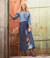 A woman in a Ventura denim skirt from Bed Stu enjoying a picture-perfect day as she leans against a wall.