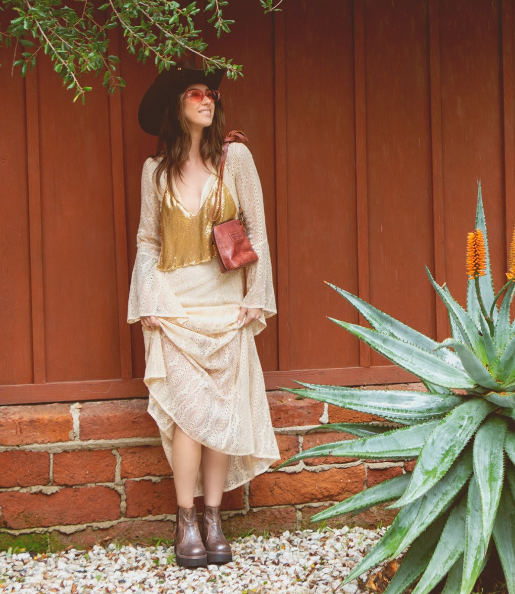 A woman wearing a Ventura hat and skirt leaning against a wall.