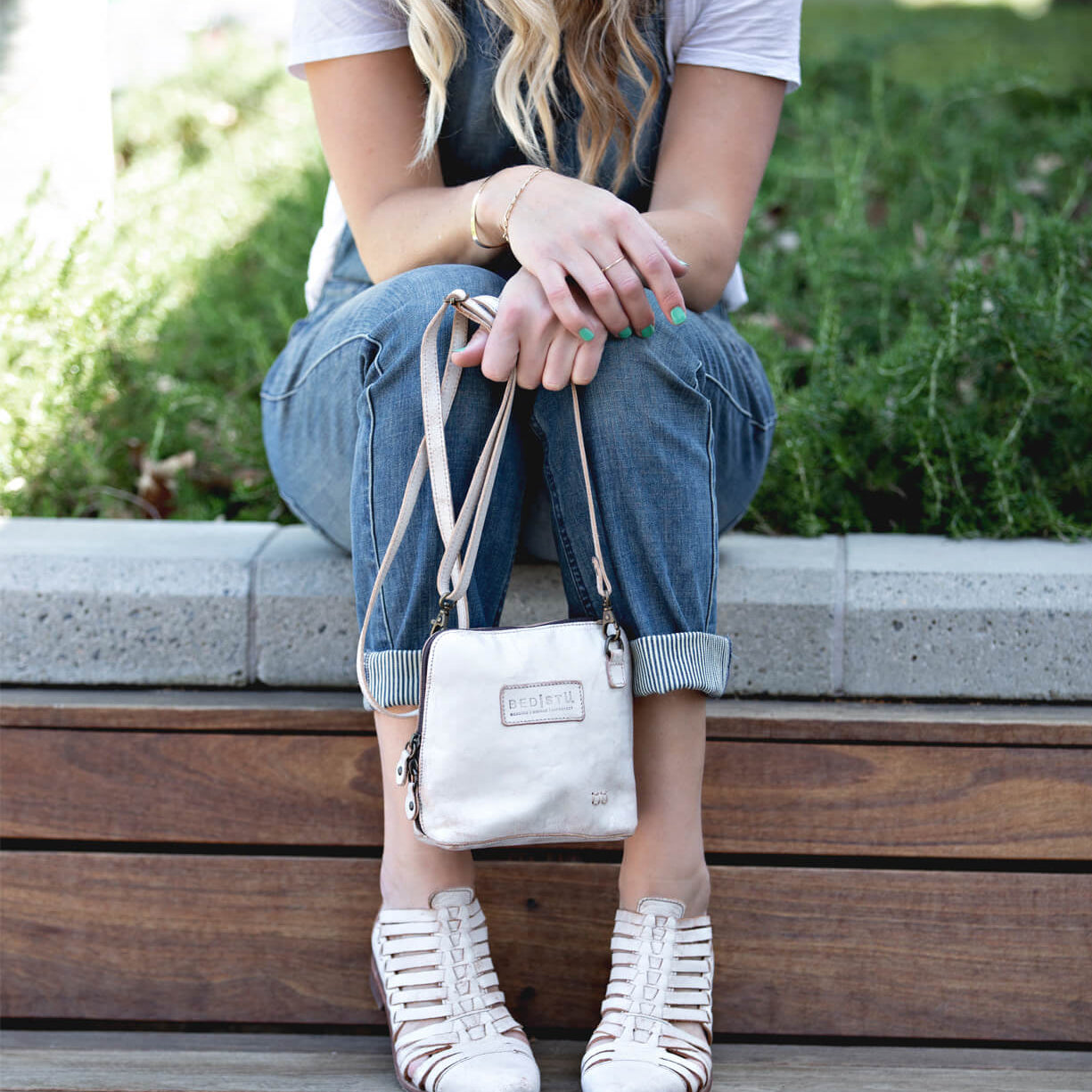 A blonde woman sitting on a bench holding a white Ventura purse by Bed Stu.