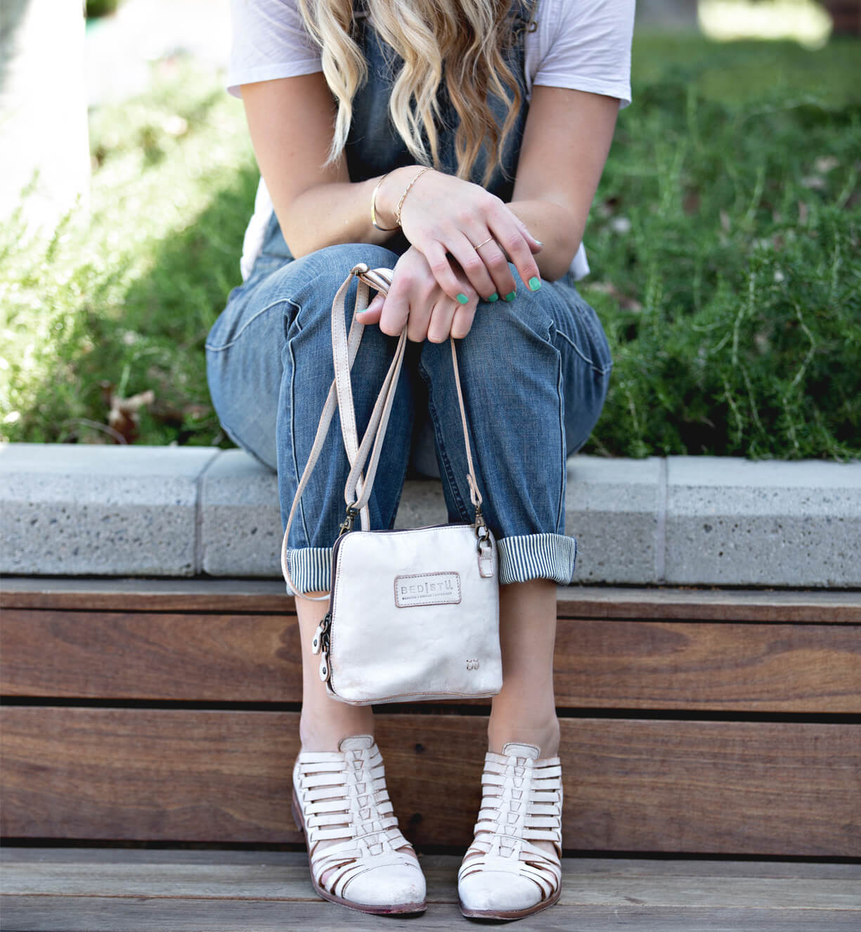 A blonde woman sitting on a bench holding a white Ventura purse by Bed Stu.