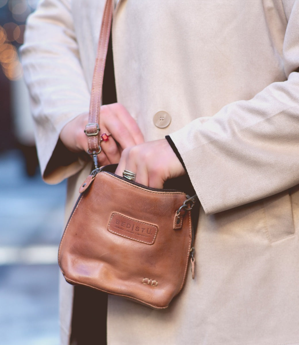 A woman wearing a trench coat holding a Bed Stu Ventura tan leather bag.