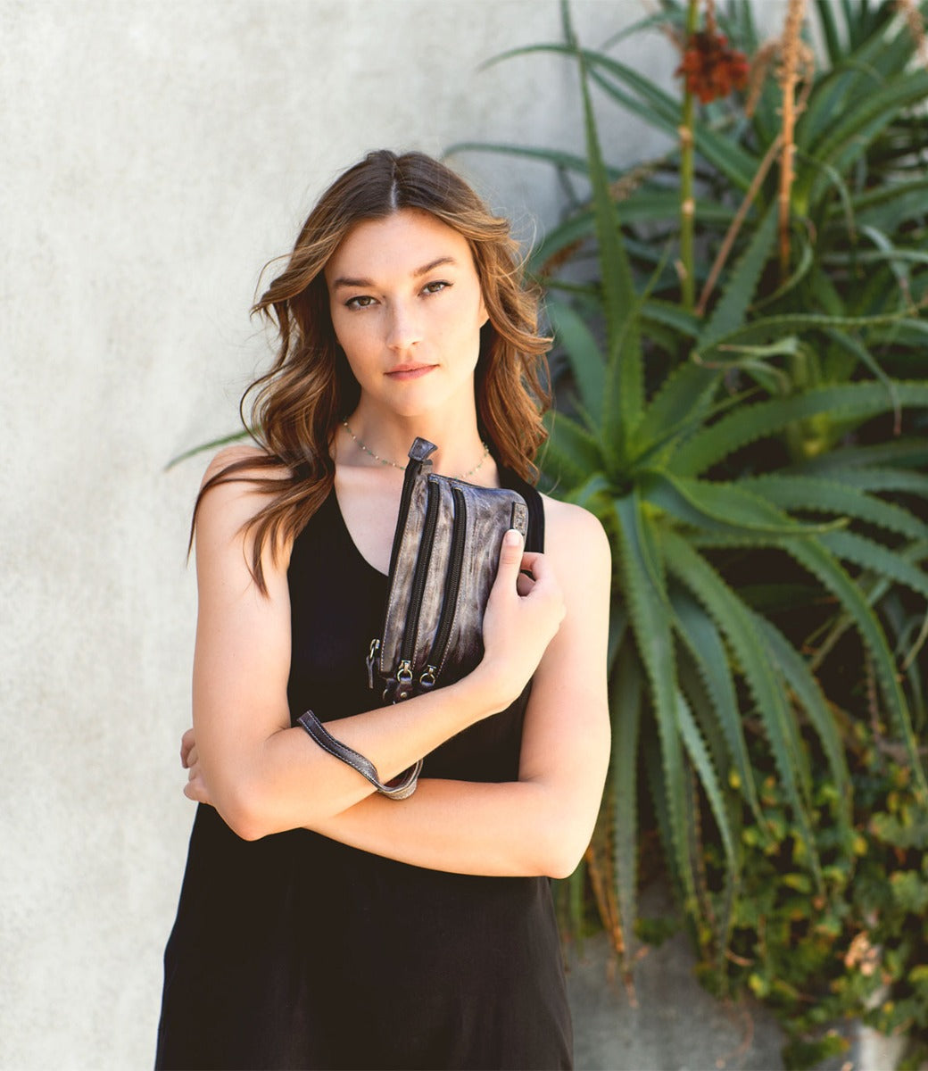 A woman wearing a black Viana dress and Bed Stu clutch.