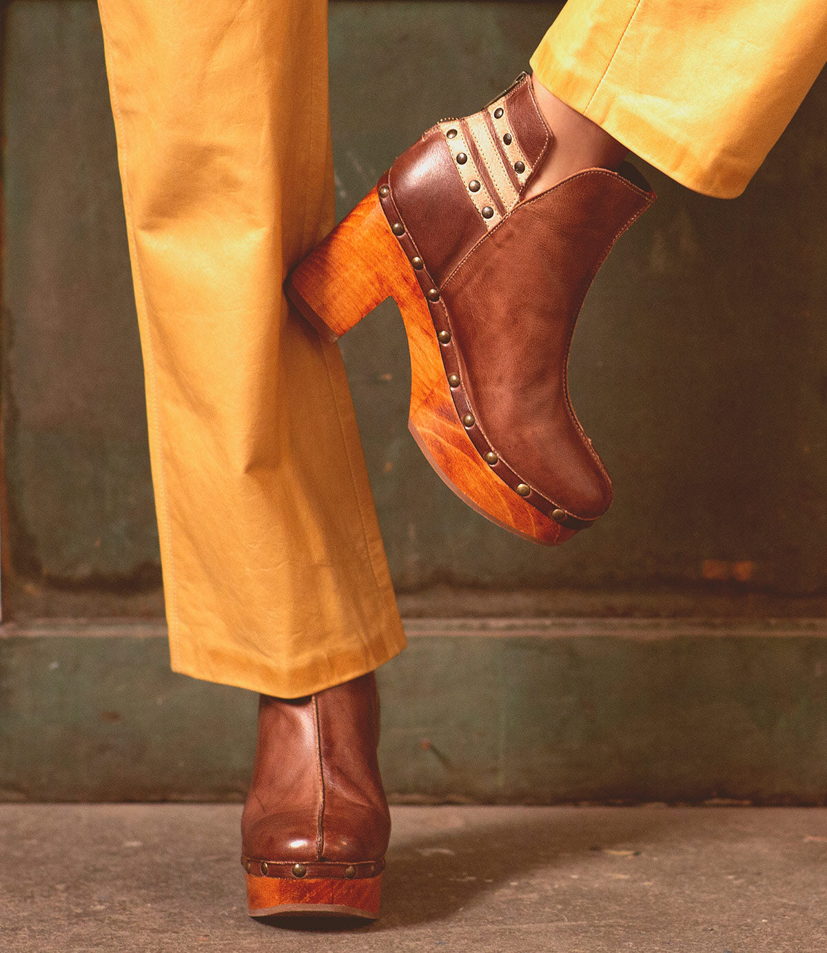 A woman wearing yellow Viena pants and brown leather Bed Stu booties with stud detail.