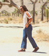 A man is walking in the desert with a Bed Stu Wizard skateboard.