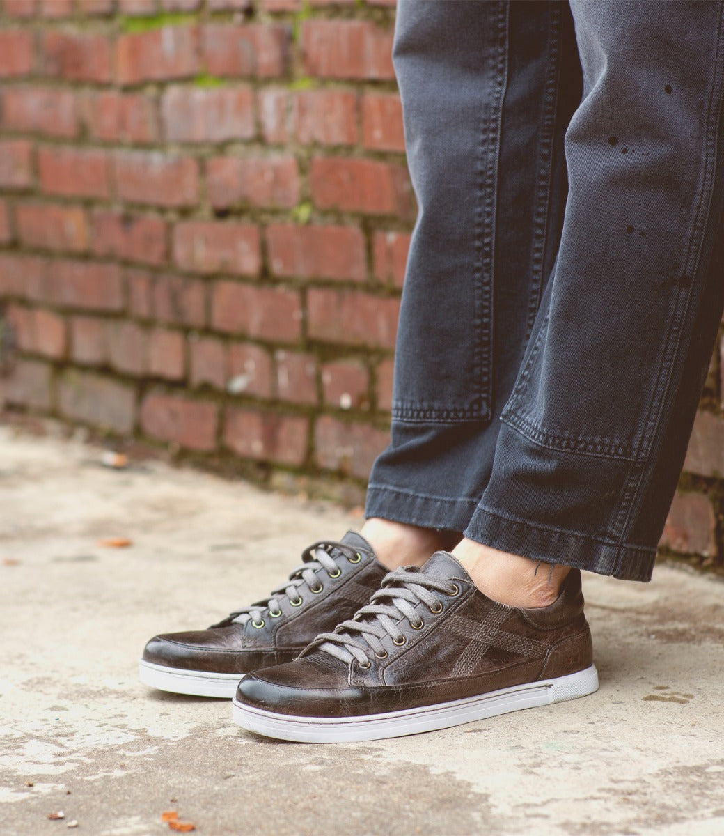 A person standing on a brick wall wearing a pair of Bed Stu sneakers.