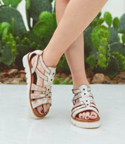 A woman wearing white Bed Stu sandals called Wonder in front of a cactus.