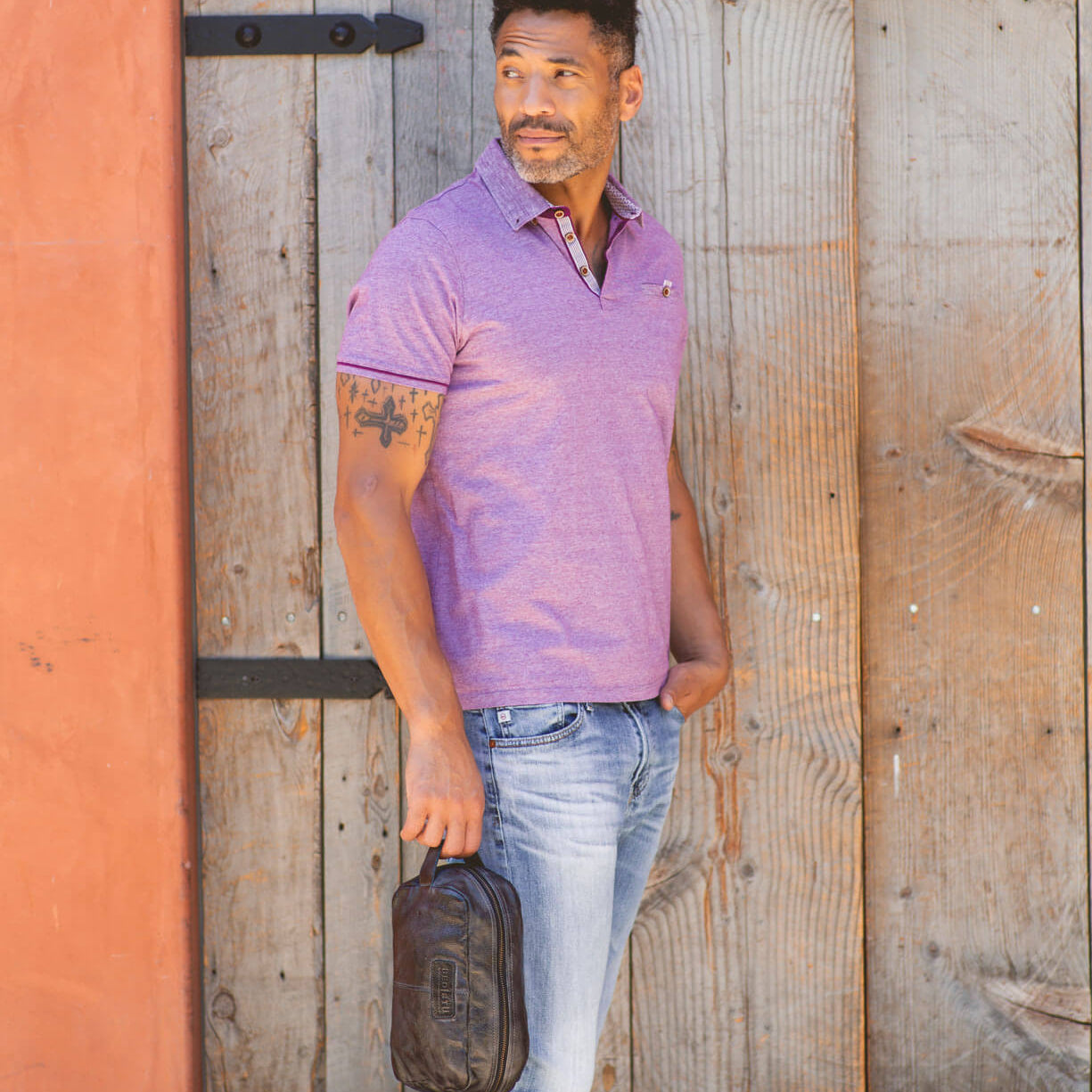 A man in a Yatra polo shirt leaning against a wooden wall. (Brand: Bed Stu)