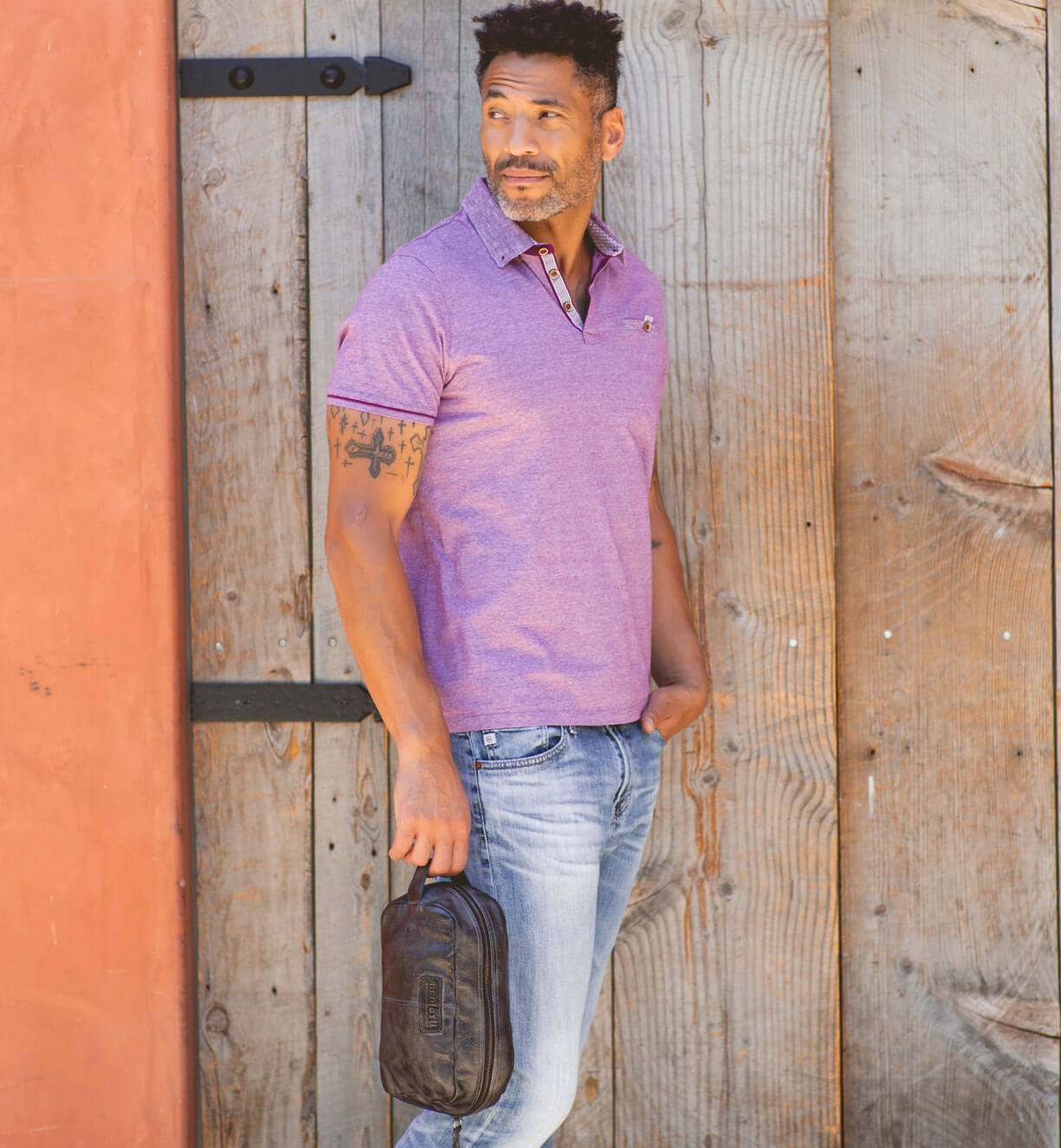 A man in a Yatra polo shirt leaning against a wooden wall. (Brand: Bed Stu)