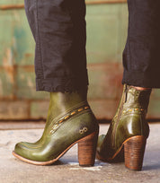A woman wearing green leather Yuno ankle boots by Bed Stu with a heel.