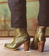 A woman wearing green leather Yuno ankle boots by Bed Stu with a heel.