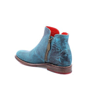 The Yurisa by Bed Stu is a timeless turquoise leather ankle boot with a textured finish, featuring a side zipper and a wooden sole. The interior lining is red, making it perfect for everyday wear.