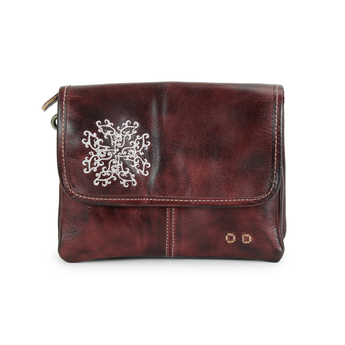 The Bed Stu Ziggy JB is a dark brown leather clutch featuring a silver snowflake design, two small gold studs on the front flap, and delicate embroidered details for an elegant touch.