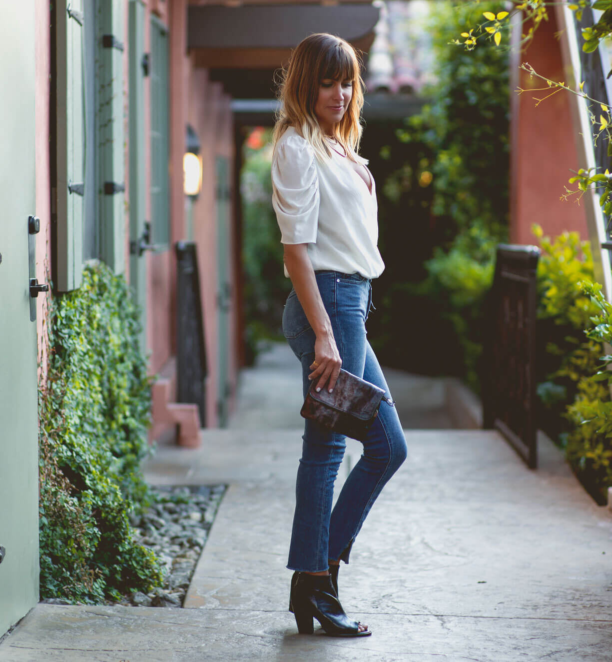 A woman wearing jeans, white blouse and a Bed Stu black and brown Ziggy clutch.