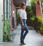 A woman wearing jeans, white blouse and a Bed Stu black and brown Ziggy clutch.