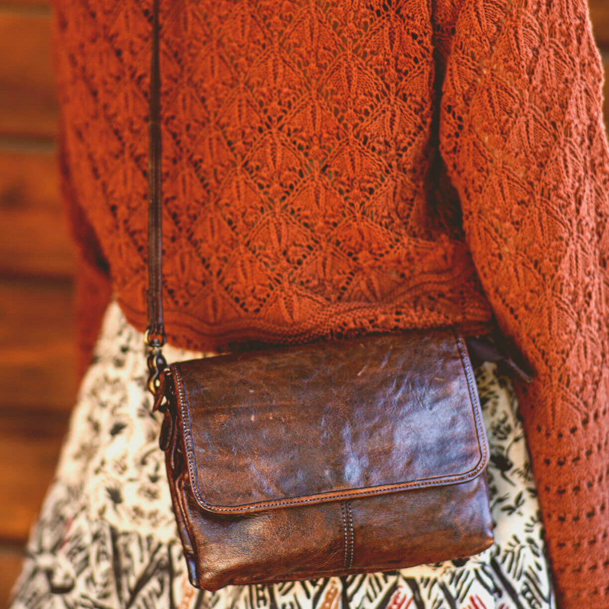 A woman is holding a brown leather Bed Stu Ziggy cross body bag.