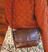 A woman is holding a brown leather Bed Stu Ziggy cross body bag.