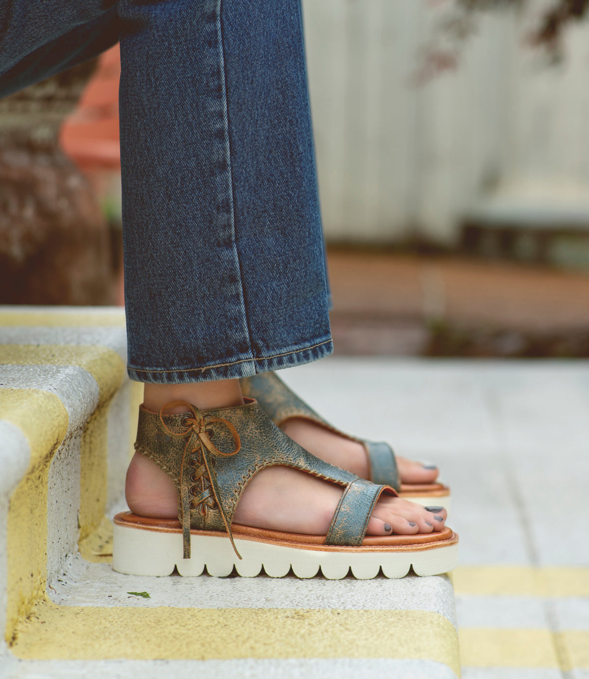 A woman wearing Bed Stu jeans and Bed Stu sandals standing on steps.